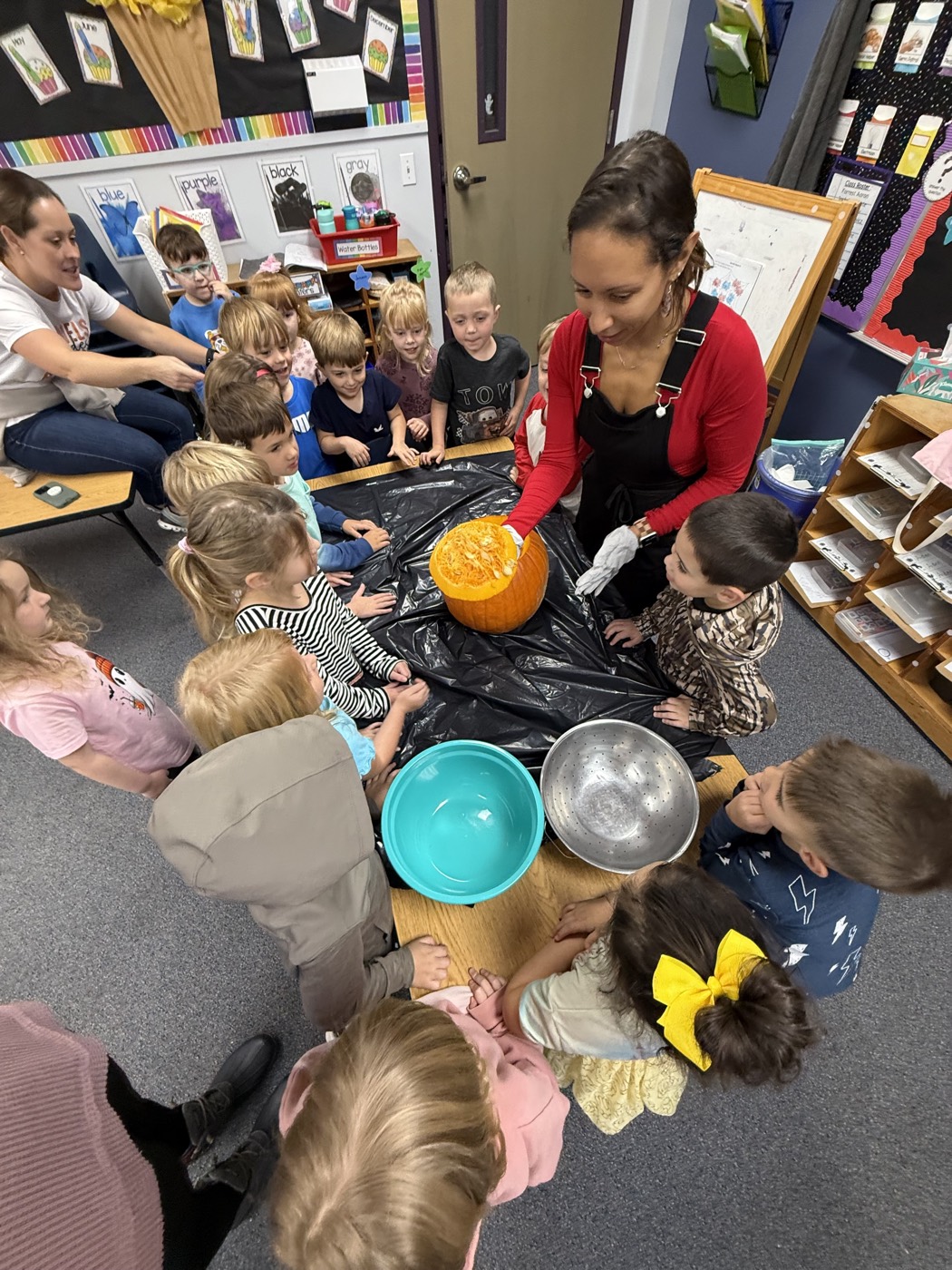 A teacher and preschoolers gathered around a table carving a pumpkin together
