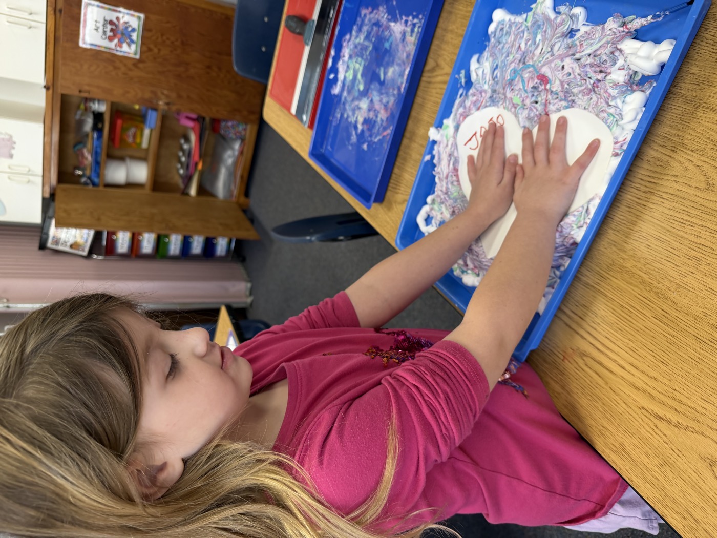 A preschooler making a handprint in shaving cream at the classroom art center